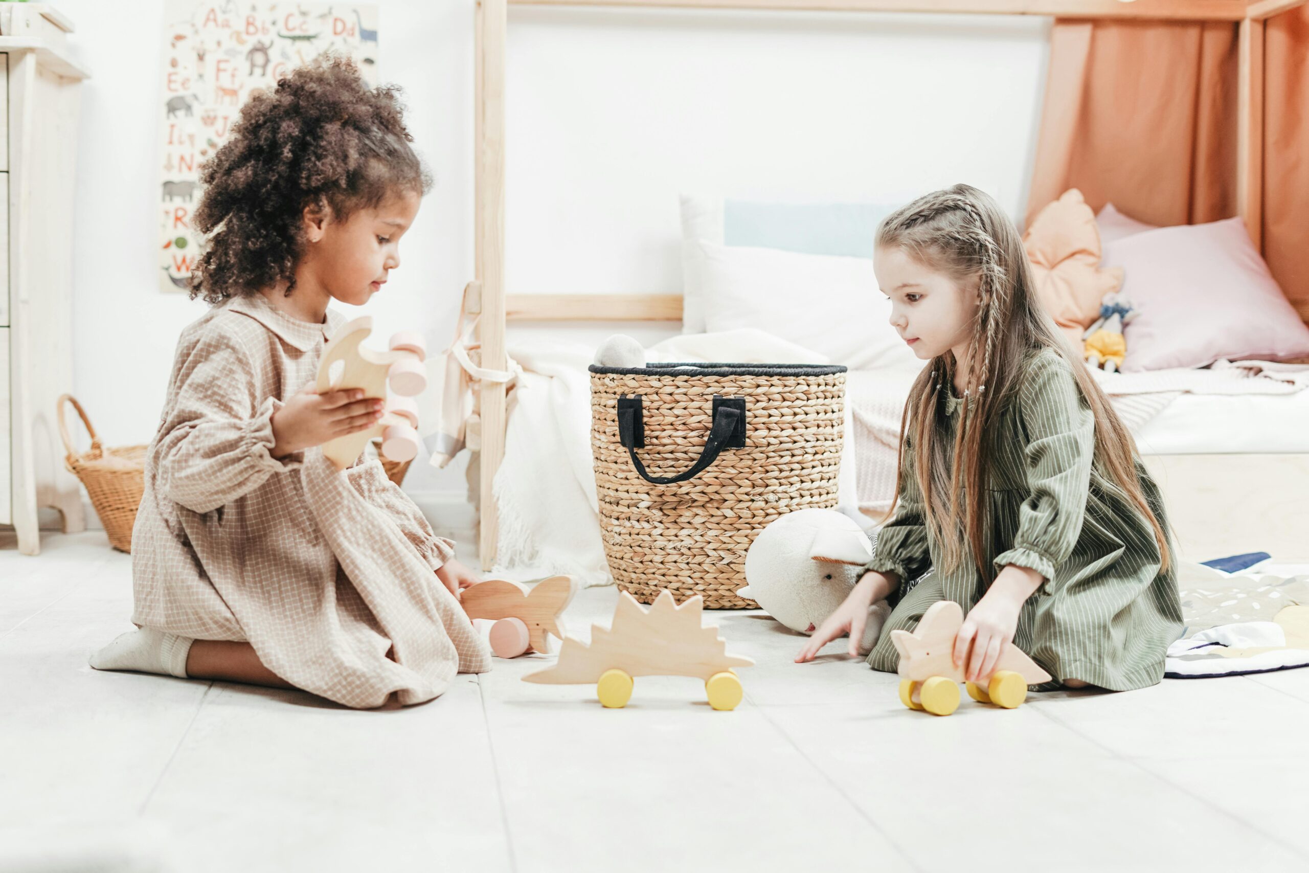 two four year old girls playing together with wooden animals on wheels to meet their play milestones in early childhood