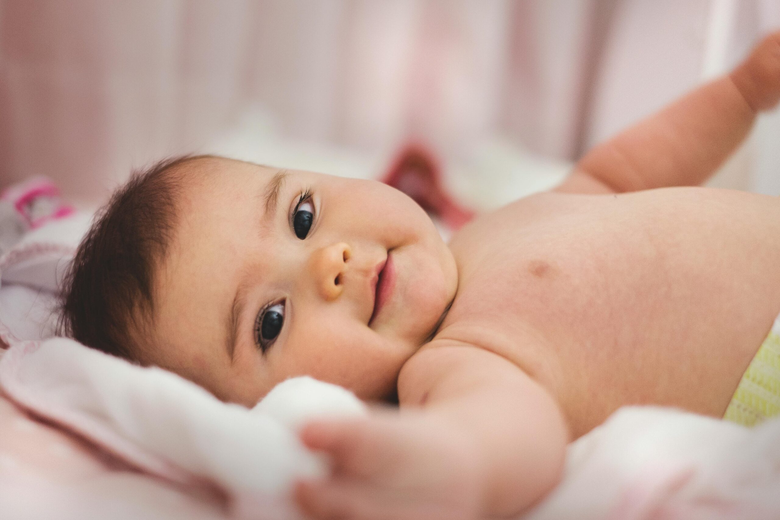 infant laying on a soft blanket to promote their early childhood development while reaching toward the camera with a smile on their face